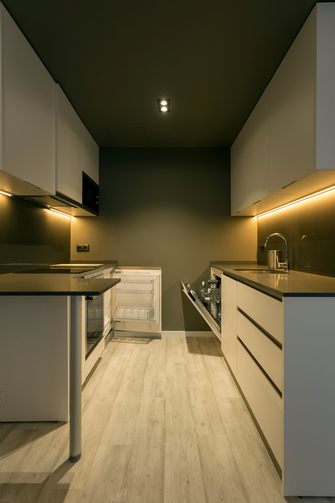 На фото: параллельная кухня-гостиная среднего размера в современном стиле с одинарной мойкой, плоскими фасадами, белыми фасадами, черным фартуком и светлым паркетным полом без острова с