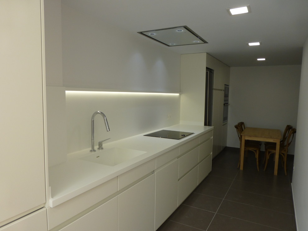 Foto på ett mellanstort funkis linjärt kök och matrum, med en integrerad diskho, släta luckor, vita skåp, vitt stänkskydd, rostfria vitvaror och klinkergolv i keramik