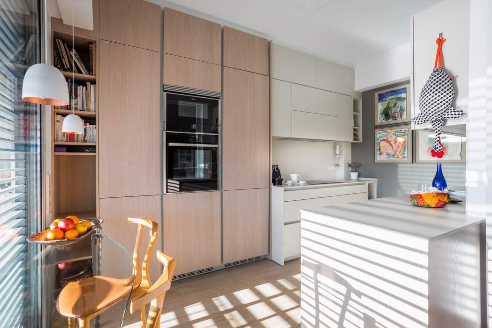 Design ideas for a medium sized contemporary galley enclosed kitchen in Barcelona with no island, flat-panel cabinets, light wood cabinets, black appliances, light hardwood flooring, beige floors and white worktops.