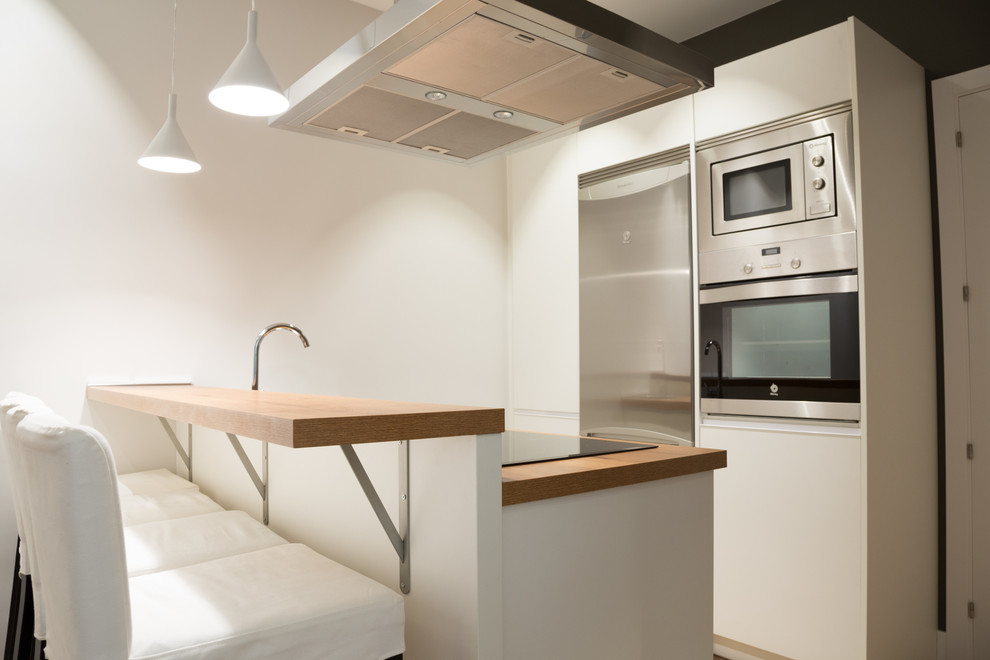 Источник вдохновения для домашнего уюта: параллельная кухня-гостиная среднего размера в скандинавском стиле с плоскими фасадами, белыми фасадами, деревянной столешницей, техникой из нержавеющей стали и полуостровом