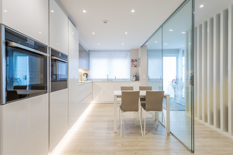 Trendy l-shaped light wood floor and beige floor eat-in kitchen photo in Other with an undermount sink, flat-panel cabinets, white cabinets, white backsplash, stainless steel appliances, no island and white countertops