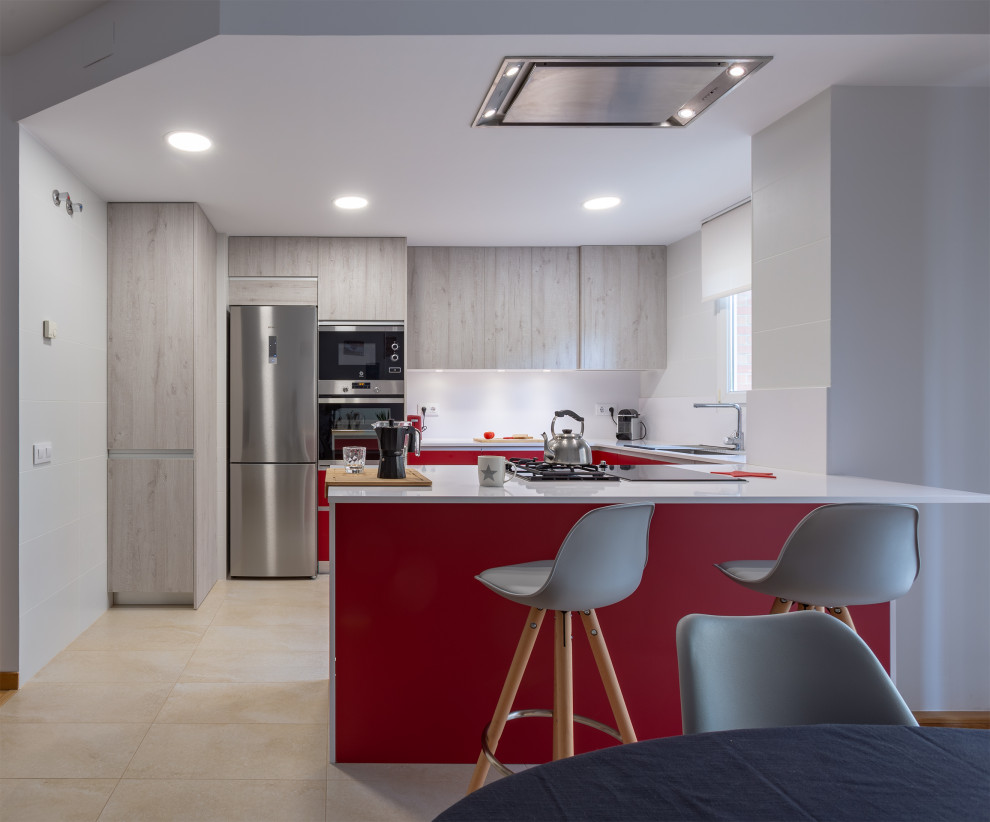 Design ideas for a medium sized contemporary u-shaped open plan kitchen in Barcelona with a double-bowl sink, flat-panel cabinets, red cabinets, white splashback, stainless steel appliances, ceramic flooring, a breakfast bar, beige floors and white worktops.