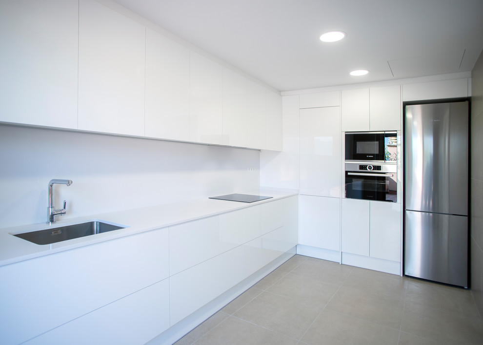 Design ideas for a large contemporary l-shaped open plan kitchen in Barcelona with a single-bowl sink, white cabinets, white splashback, stainless steel appliances, ceramic flooring, no island, beige floors and white worktops.