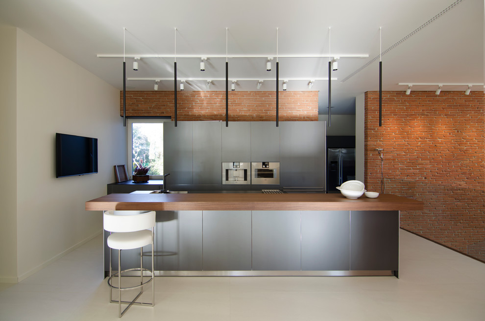 Imagen de cocina lineal contemporánea grande abierta con armarios con paneles lisos, puertas de armario grises, encimera de madera y electrodomésticos de acero inoxidable