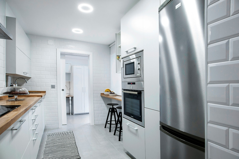 Design ideas for a medium sized scandinavian galley enclosed kitchen in Other with flat-panel cabinets, white cabinets, wood worktops, white splashback, metro tiled splashback, ceramic flooring and no island.