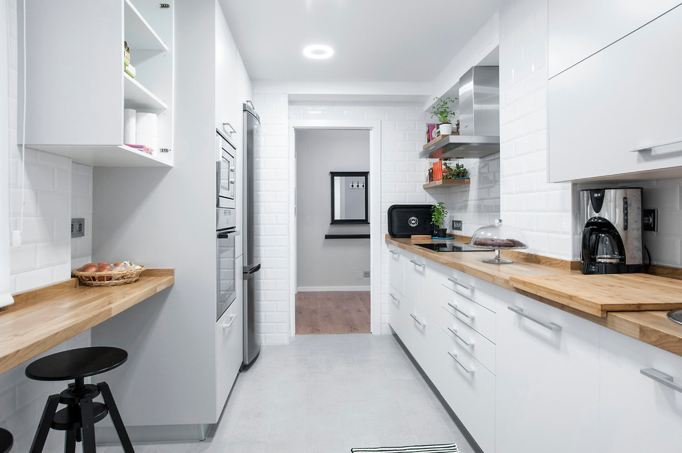 Ejemplo de cocina escandinava de tamaño medio cerrada sin isla con armarios con paneles lisos, puertas de armario blancas, encimera de madera, salpicadero blanco, salpicadero de azulejos tipo metro y electrodomésticos de acero inoxidable