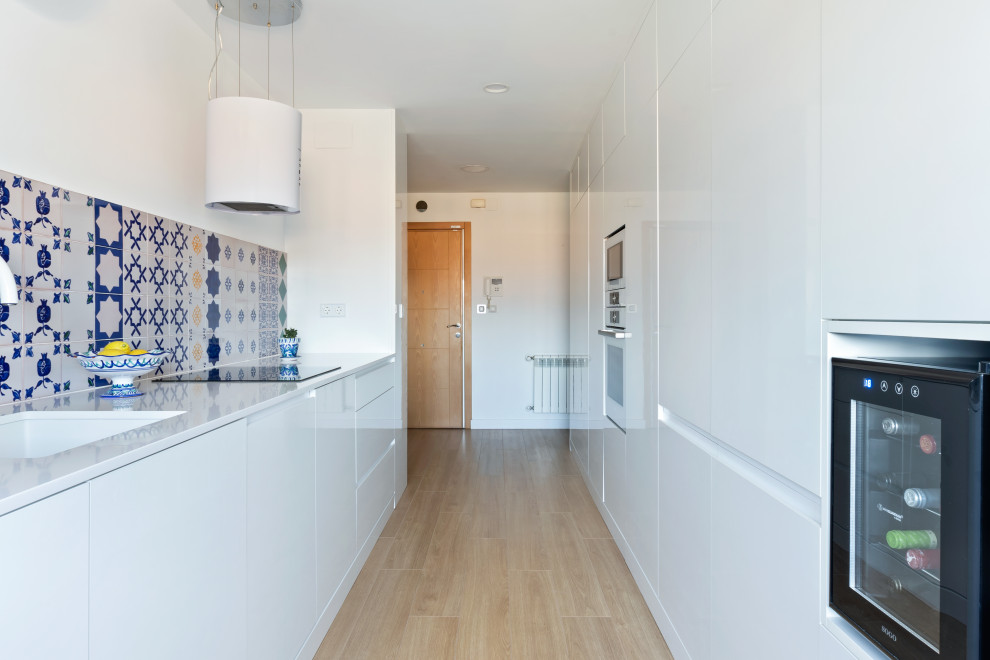 Exempel på ett mellanstort medelhavsstil vit linjärt vitt kök med öppen planlösning, med en undermonterad diskho, släta luckor, vita skåp, bänkskiva i kvarts, vita vitvaror och laminatgolv