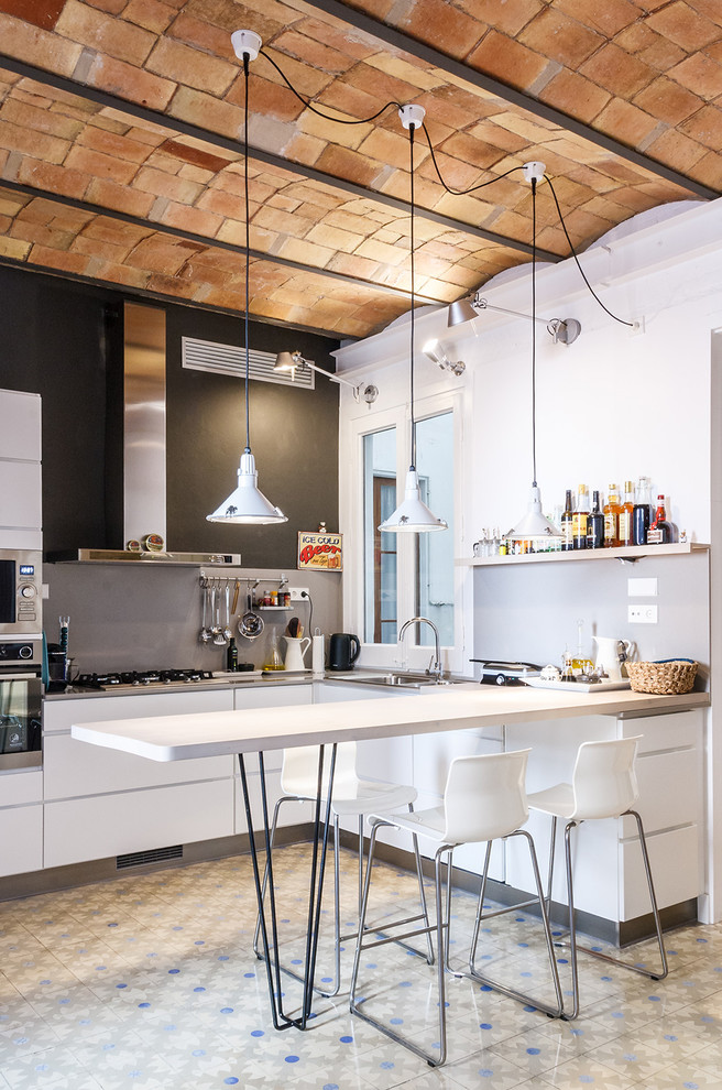 Photo of a medium sized industrial u-shaped open plan kitchen in Barcelona with flat-panel cabinets, white cabinets, grey splashback, stainless steel appliances, ceramic flooring and a breakfast bar.