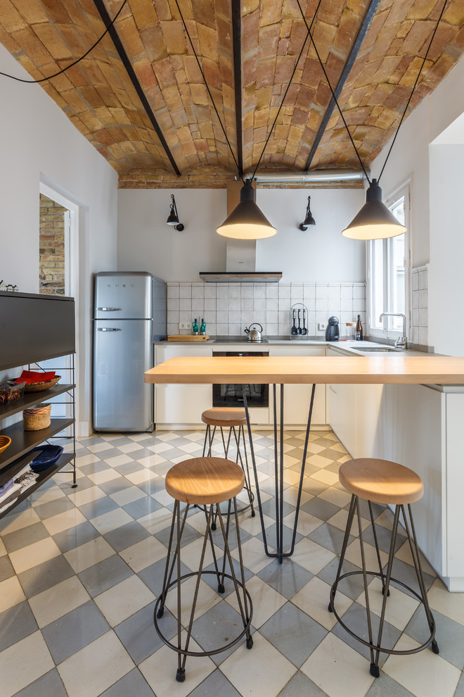 Mittelgroße Moderne Küche in L-Form mit flächenbündigen Schrankfronten, weißen Schränken, Küchenrückwand in Weiß, Küchengeräten aus Edelstahl, Halbinsel und grauem Boden in Barcelona