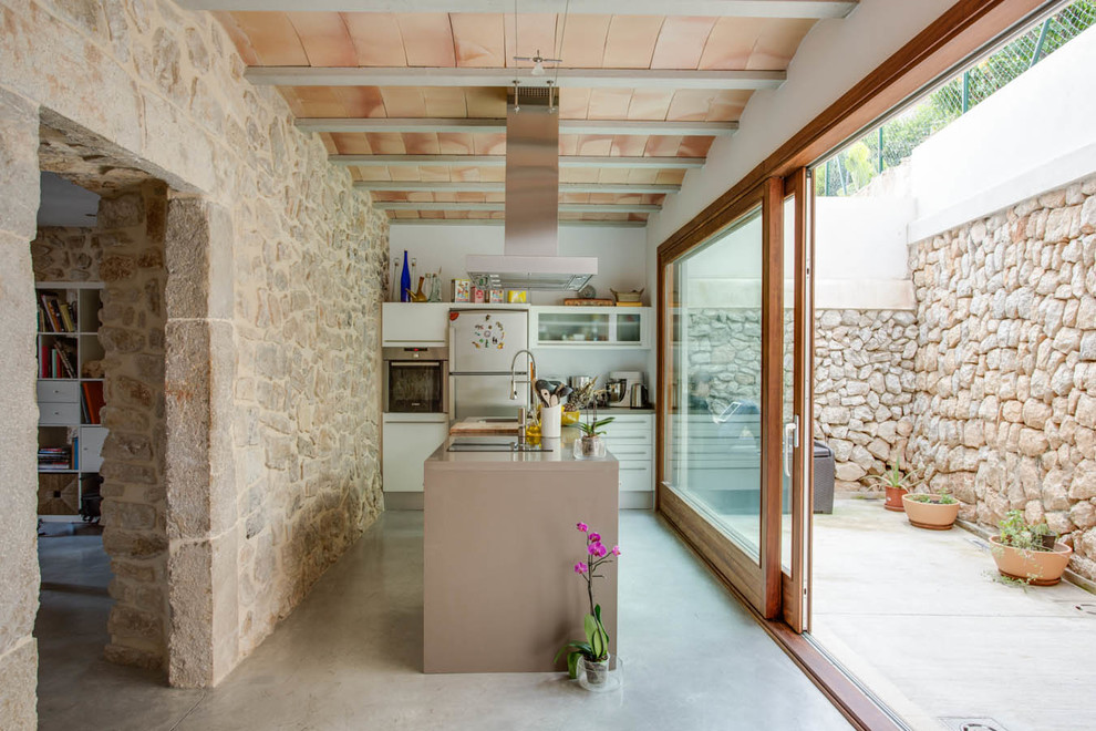 Идея дизайна: маленькая прямая кухня-гостиная в средиземноморском стиле с плоскими фасадами, белыми фасадами, белым фартуком, техникой из нержавеющей стали, бетонным полом и островом для на участке и в саду