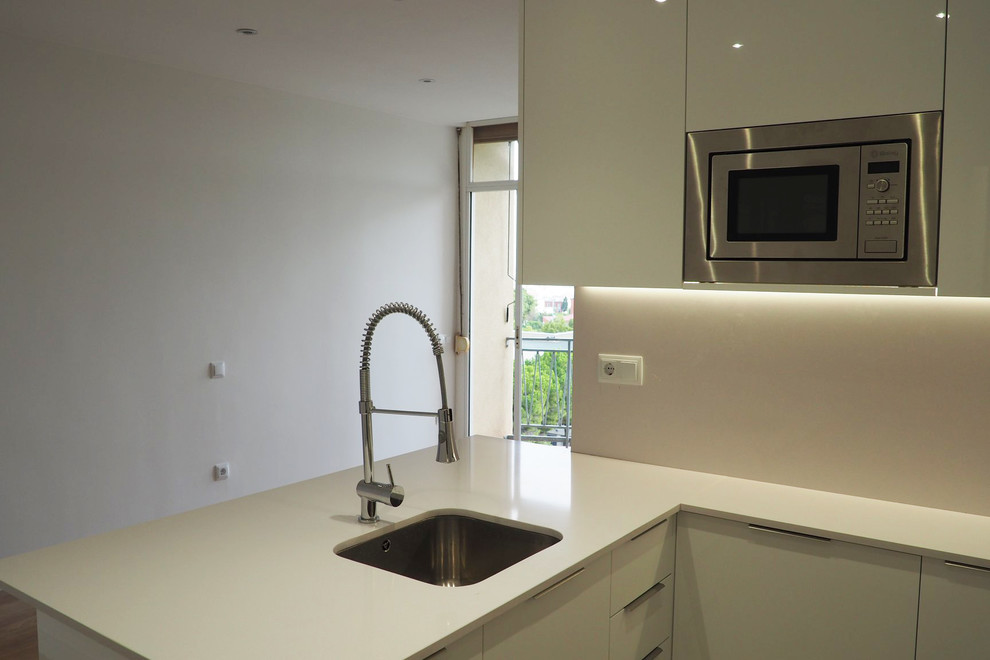 This is an example of a medium sized contemporary u-shaped open plan kitchen in Barcelona with a single-bowl sink, flat-panel cabinets, white cabinets, white splashback, stainless steel appliances, ceramic flooring, no island, grey floors and white worktops.