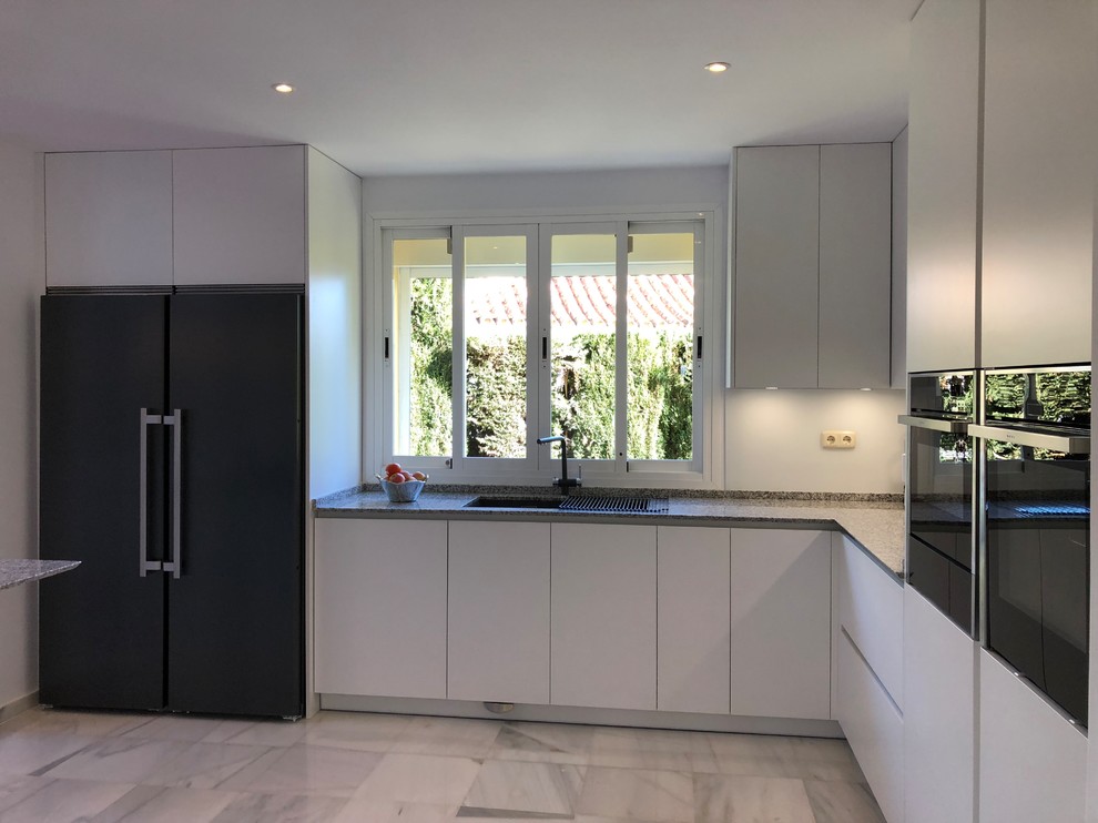 Large modern open plan kitchen in Other with a double-bowl sink, flat-panel cabinets, white cabinets, granite worktops, white splashback, window splashback, black appliances, marble flooring, a breakfast bar, white floors and grey worktops.