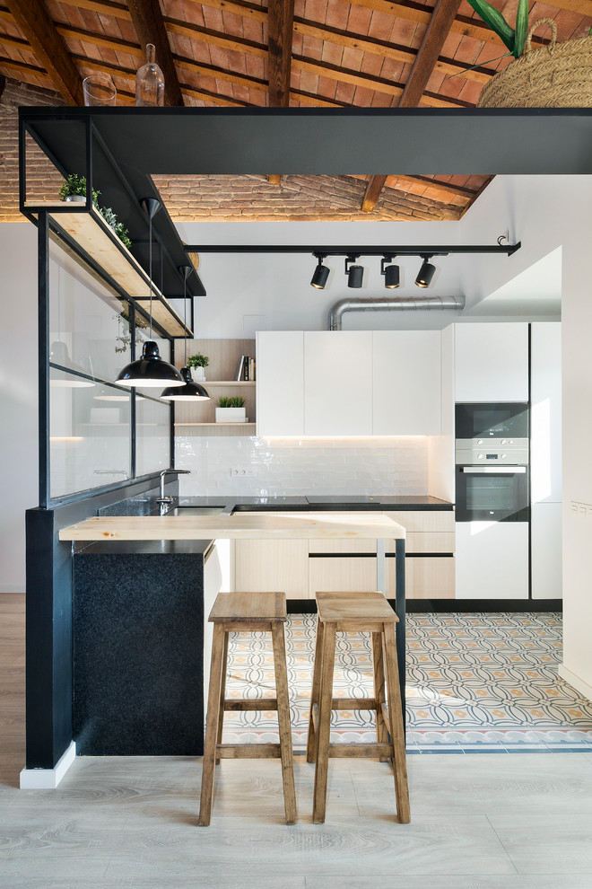 This is an example of a small industrial u-shaped enclosed kitchen in Barcelona with light hardwood flooring, flat-panel cabinets, white cabinets, white splashback, metro tiled splashback, stainless steel appliances and a breakfast bar.