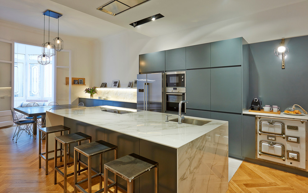 Diseño de cocina lineal contemporánea grande abierta con armarios con paneles lisos, una isla, fregadero bajoencimera, puertas de armario azules, electrodomésticos de acero inoxidable y suelo de madera clara