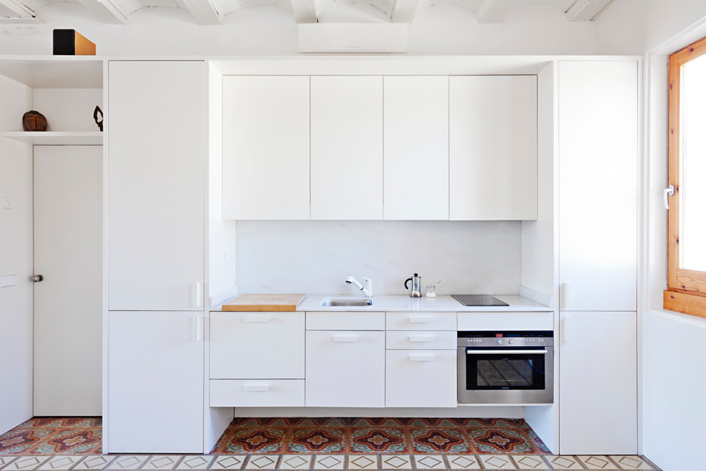 Idéer för ett litet medelhavsstil vit linjärt kök, med en enkel diskho, släta luckor, marmorbänkskiva, vitt stänkskydd, stänkskydd i marmor, cementgolv, vita skåp, rostfria vitvaror och flerfärgat golv
