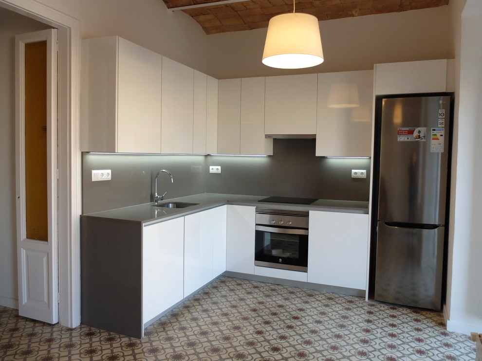 This is an example of a medium sized traditional l-shaped kitchen/diner in Barcelona with a single-bowl sink, flat-panel cabinets, white cabinets, engineered stone countertops, grey splashback, stainless steel appliances, terracotta flooring and no island.