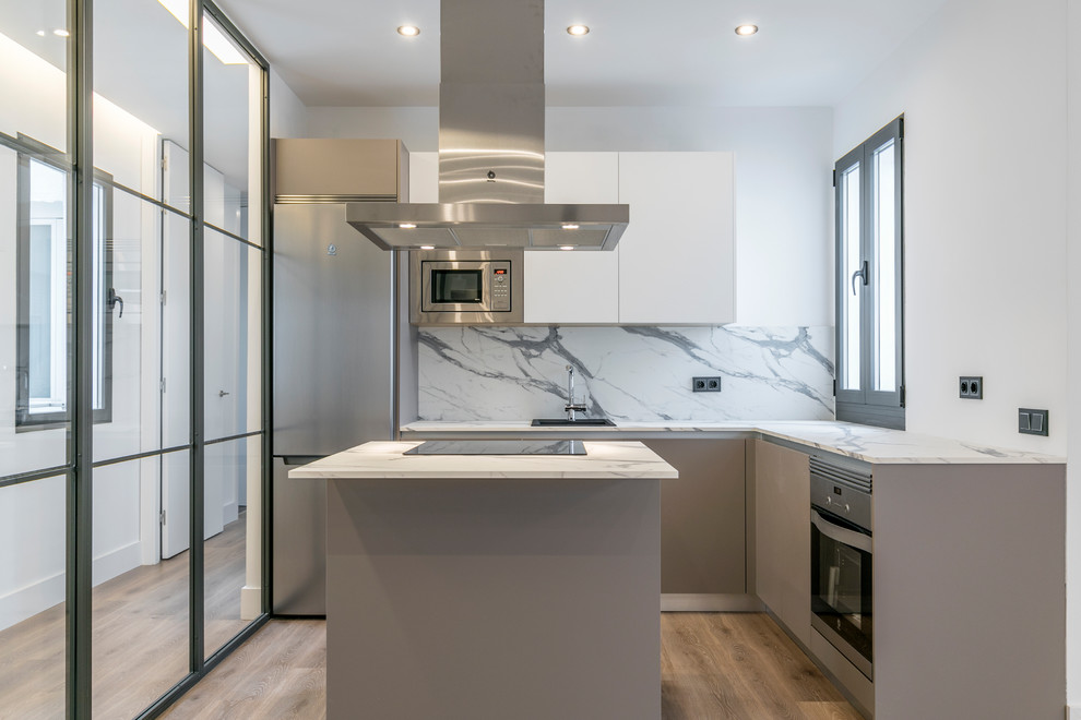 Moderne Küche in L-Form mit Einbauwaschbecken, flächenbündigen Schrankfronten, weißen Schränken, Küchenrückwand in Weiß, Küchengeräten aus Edelstahl, braunem Holzboden, Kücheninsel, braunem Boden und weißer Arbeitsplatte in Madrid