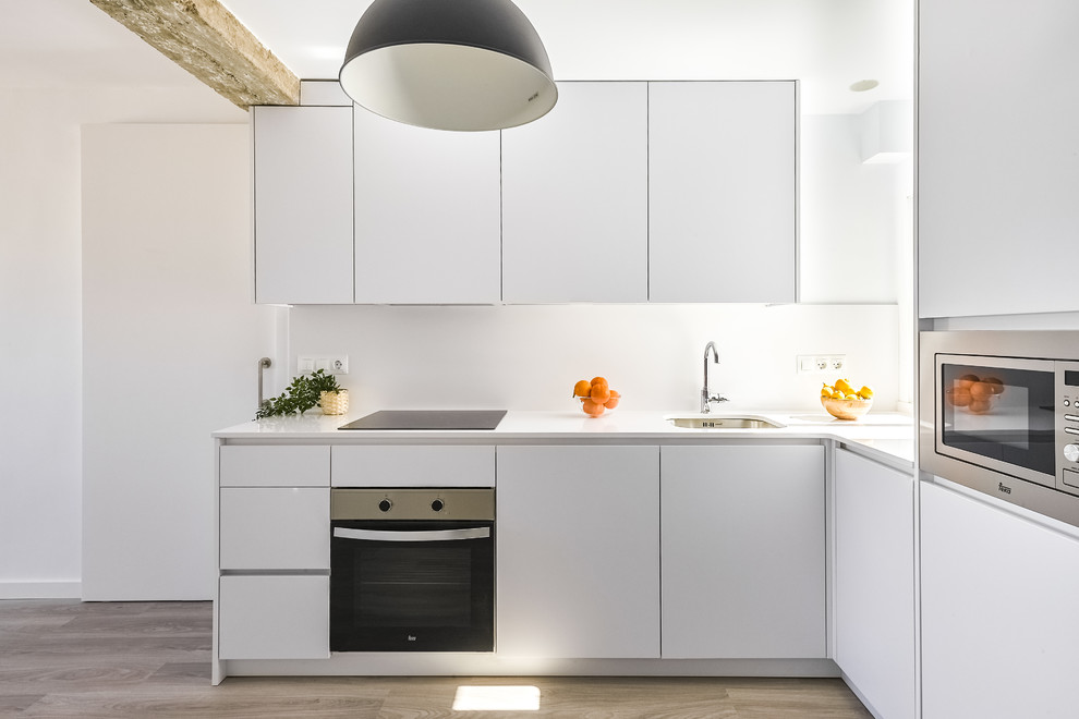 Medium sized contemporary l-shaped kitchen/diner in Valencia with a submerged sink, flat-panel cabinets, white cabinets, engineered stone countertops, white splashback, integrated appliances, laminate floors, no island, brown floors and white worktops.