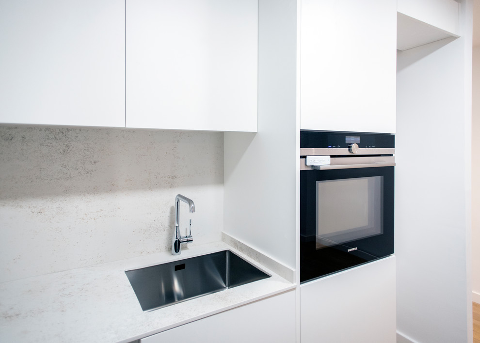 Inspiration för mellanstora moderna vitt kök, med en enkel diskho, släta luckor, vita skåp, vitt stänkskydd, rostfria vitvaror, mellanmörkt trägolv och brunt golv