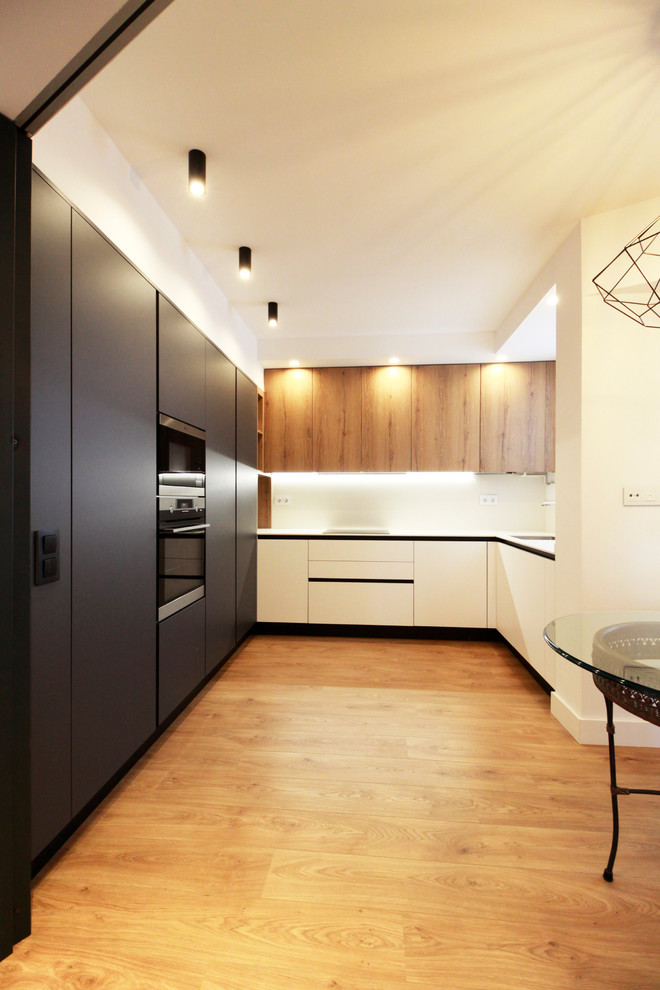 Diseño de cocina contemporánea grande con armarios con paneles lisos, puertas de armario negras, salpicadero blanco, suelo laminado y electrodomésticos negros