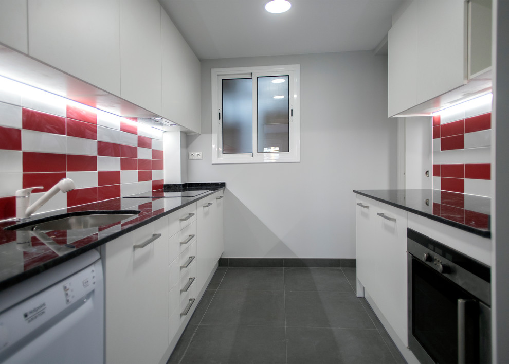 Cette image montre une cuisine parallèle design fermée et de taille moyenne avec un évier 1 bac, des portes de placard blanches, une crédence rouge, un électroménager en acier inoxydable, aucun îlot, un sol gris et plan de travail noir.