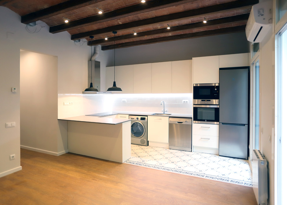 Design ideas for a medium sized contemporary u-shaped open plan kitchen in Barcelona with a single-bowl sink, white cabinets, white splashback, ceramic splashback, stainless steel appliances and white floors.