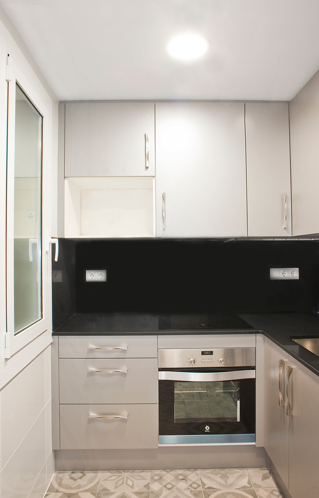 Ejemplo de cocinas en L clásica renovada pequeña cerrada con salpicadero negro y armarios con paneles lisos