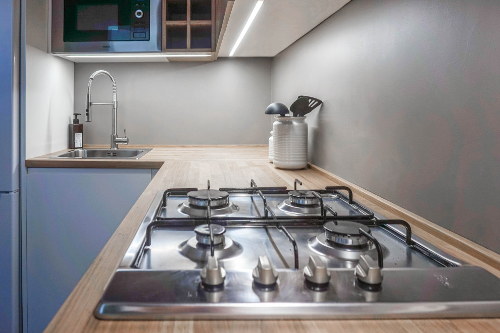 Bild på ett litet nordiskt beige beige kök, med en enkel diskho, släta luckor, skåp i mellenmörkt trä, träbänkskiva, grått stänkskydd, stänkskydd i cementkakel, vita vitvaror, betonggolv och svart golv