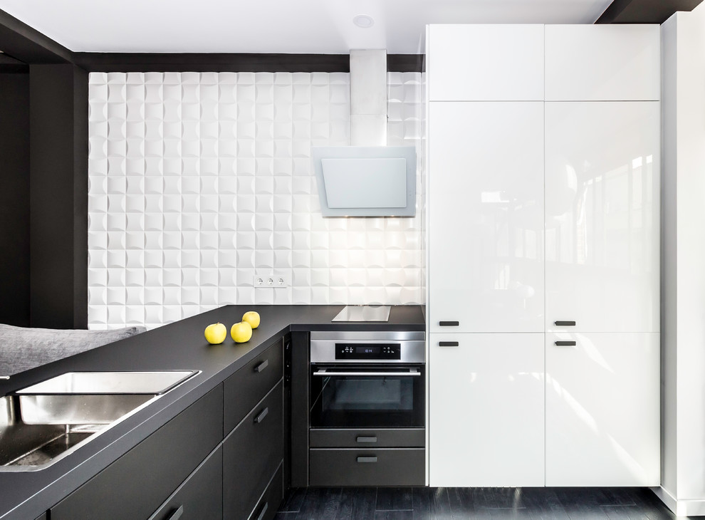 На фото: угловая кухня-гостиная среднего размера в современном стиле с плоскими фасадами, черными фасадами и белым фартуком без острова