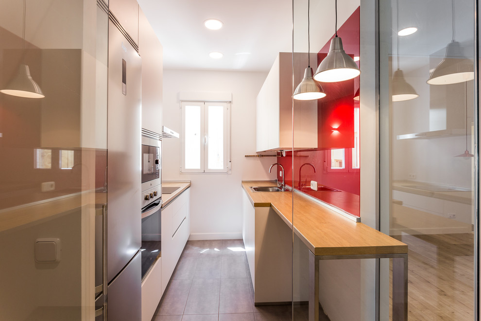 Cette photo montre une cuisine parallèle scandinave fermée et de taille moyenne avec un placard à porte plane, des portes de placard blanches, un plan de travail en bois, une crédence rouge et aucun îlot.