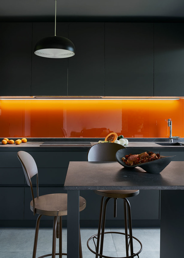 Zweizeilige, Große Moderne Küche mit Unterbauwaschbecken, flächenbündigen Schrankfronten, grauen Schränken, Küchenrückwand in Orange, Glasrückwand, Elektrogeräten mit Frontblende, Kücheninsel, grauem Boden und grauer Arbeitsplatte in Bilbao