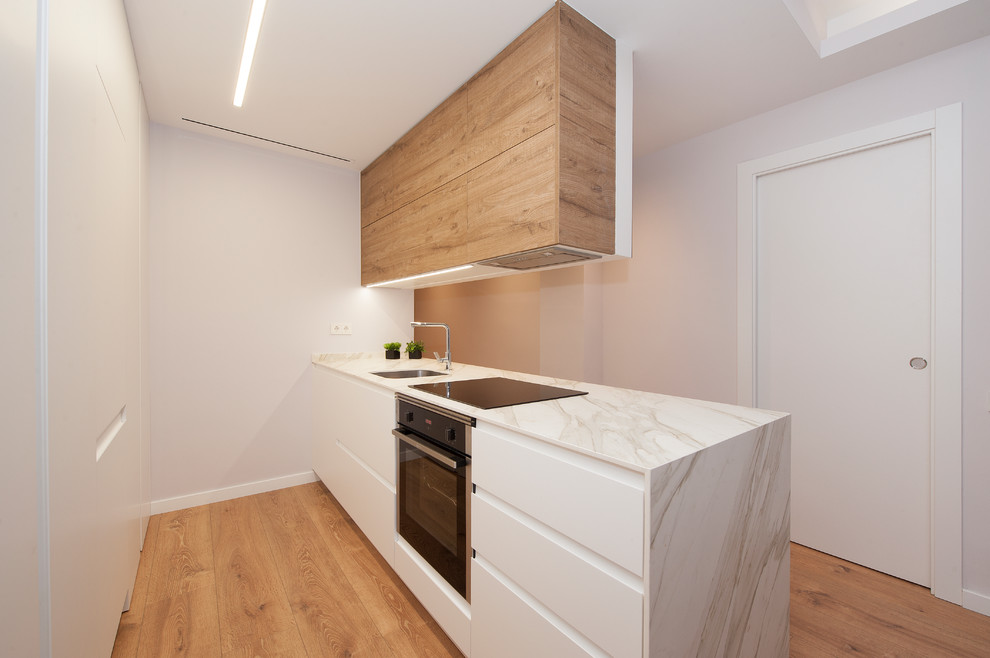Idéer för mellanstora minimalistiska vitt kök, med en enkel diskho, släta luckor, marmorbänkskiva, vitt stänkskydd, svarta vitvaror, mellanmörkt trägolv, en halv köksö och brunt golv