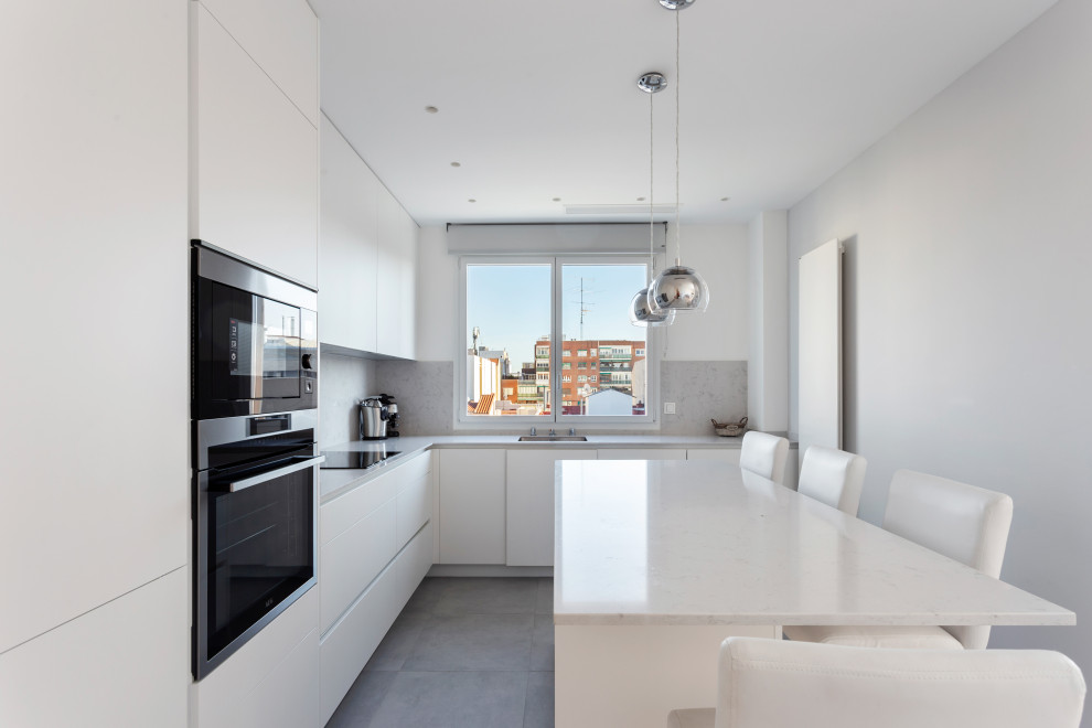 Kitchen - mid-sized contemporary l-shaped porcelain tile and gray floor kitchen idea in Madrid with an integrated sink, flat-panel cabinets, white cabinets, gray backsplash, black appliances, an island and white countertops