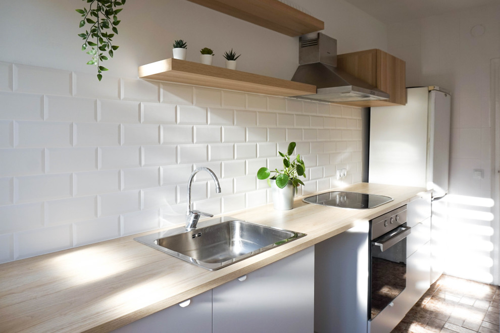 Inspiration for a mid-sized scandinavian single-wall ceramic tile and brown floor enclosed kitchen remodel in Barcelona with a single-bowl sink, flat-panel cabinets, white cabinets, laminate countertops, white backsplash, ceramic backsplash, black appliances, no island and beige countertops