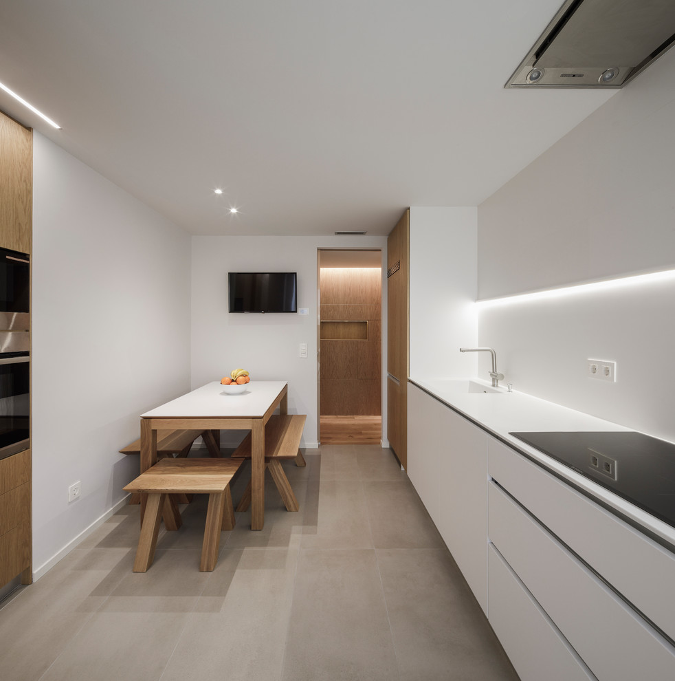 Einzeilige Moderne Wohnküche ohne Insel mit integriertem Waschbecken, flächenbündigen Schrankfronten, weißen Schränken, Küchenrückwand in Weiß, Küchengeräten aus Edelstahl, grauem Boden und weißer Arbeitsplatte in Madrid