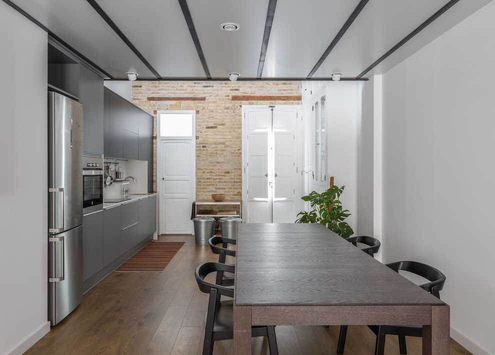 Photo of a medium sized industrial single-wall kitchen/diner in Valencia with flat-panel cabinets, grey cabinets, white splashback, dark hardwood flooring, no island and brown floors.
