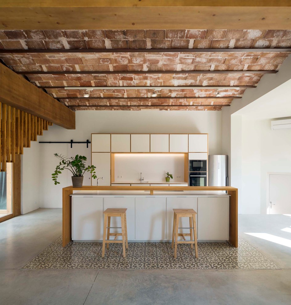 Example of a large tuscan single-wall concrete floor and gray floor open concept kitchen design in Barcelona with flat-panel cabinets, white cabinets, wood countertops, white backsplash, stainless steel appliances and an island