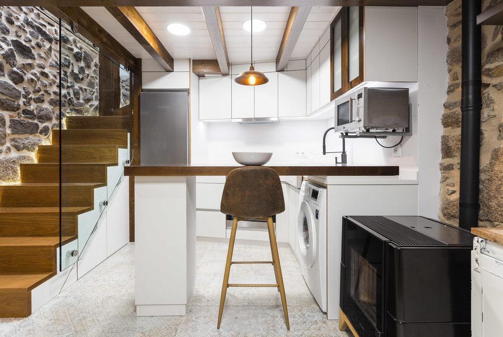 Urban l-shaped enclosed kitchen in Other with flat-panel cabinets, white cabinets, wood worktops, white splashback, stainless steel appliances, cement flooring, a breakfast bar, beige floors and brown worktops.