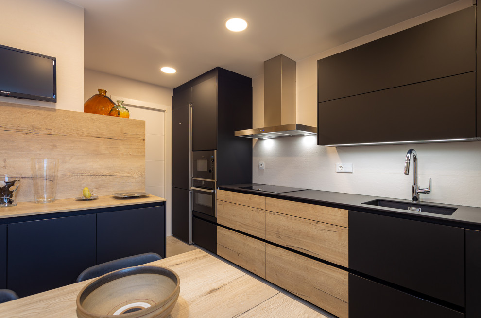 Cette photo montre une cuisine linéaire tendance fermée et de taille moyenne avec un évier 1 bac, des portes de placard noires, un électroménager noir, un sol en carrelage de céramique et un sol gris.