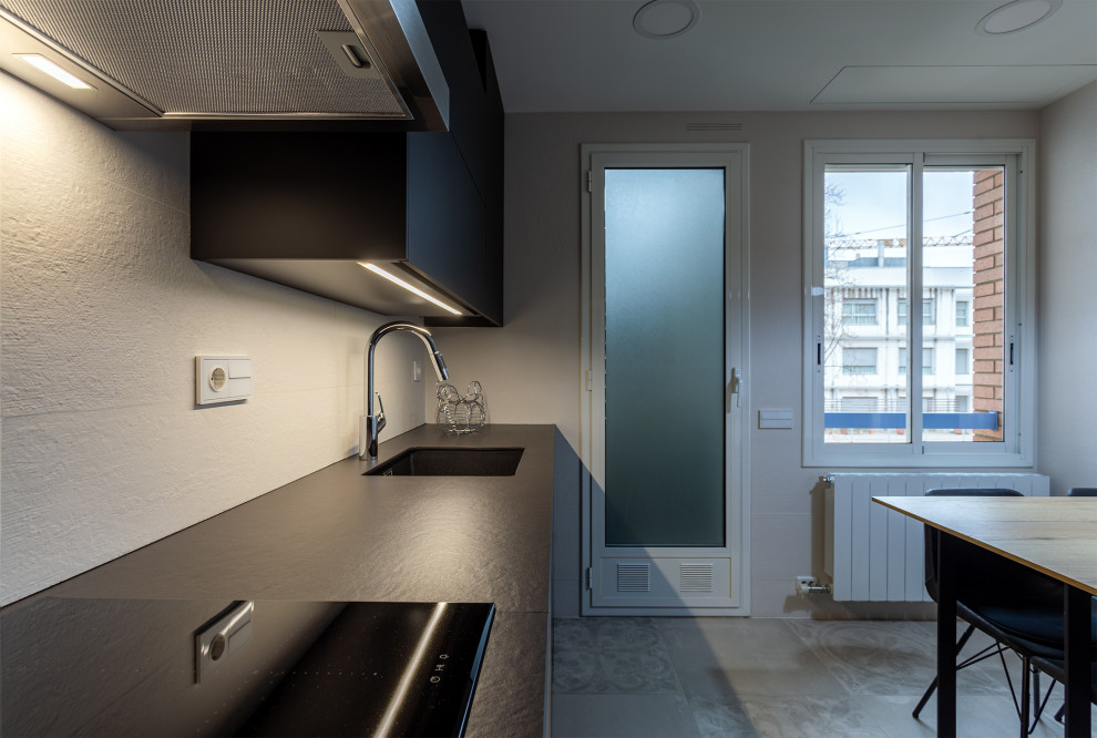 Photo of a medium sized contemporary single-wall enclosed kitchen in Barcelona with a single-bowl sink, black cabinets, beige splashback, black appliances, ceramic flooring, grey floors and black worktops.