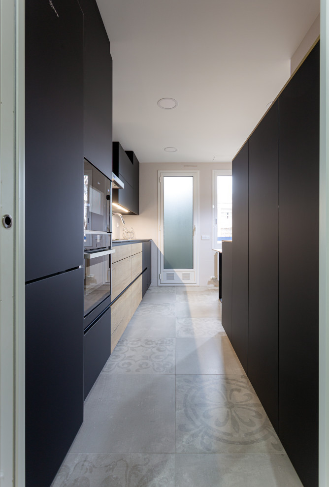 Idée de décoration pour une cuisine linéaire design fermée et de taille moyenne avec un évier 1 bac, des portes de placard noires, un électroménager noir, un sol en carrelage de céramique et un sol gris.