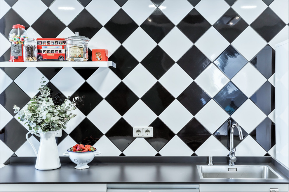 Retro inredning av ett mellanstort svart linjärt svart kök med öppen planlösning, med en rustik diskho, släta luckor, vita skåp, granitbänkskiva, vitt stänkskydd, stänkskydd i keramik, vita vitvaror, klinkergolv i porslin, en köksö och grått golv