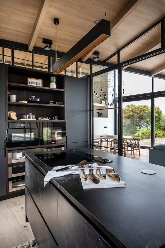 Photo of a medium sized world-inspired l-shaped enclosed kitchen in Other with flat-panel cabinets, black cabinets, porcelain flooring, an island, beige floors, black worktops and a wood ceiling.