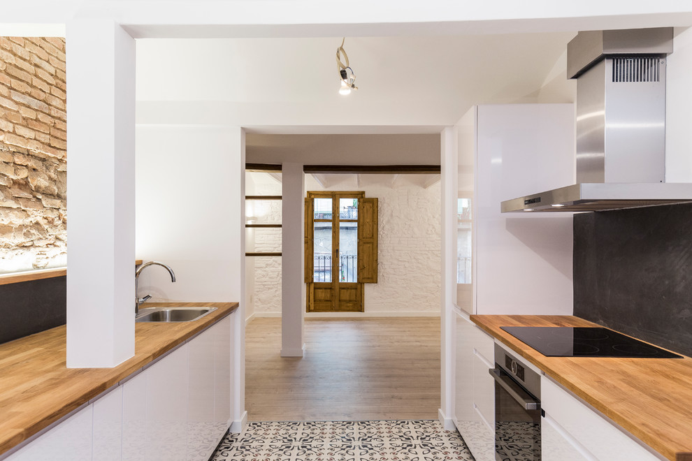 バルセロナにある小さな地中海スタイルのおしゃれなキッチン (エプロンフロントシンク、落し込みパネル扉のキャビネット、白いキャビネット、木材カウンター、黒いキッチンパネル、スレートのキッチンパネル、シルバーの調理設備、セメントタイルの床、アイランドなし、マルチカラーの床) の写真