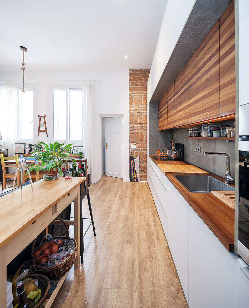 Cette photo montre une cuisine ouverte linéaire tendance en bois brun de taille moyenne avec un placard à porte plane, un plan de travail en bois, une crédence grise, un électroménager en acier inoxydable et un sol en bois brun.