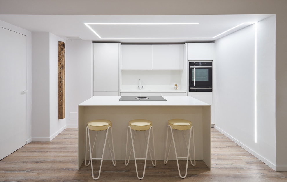 Cette image montre une cuisine linéaire design avec un placard à porte plane, des portes de placard blanches, une crédence blanche, un électroménager noir, îlot et un plan de travail blanc.