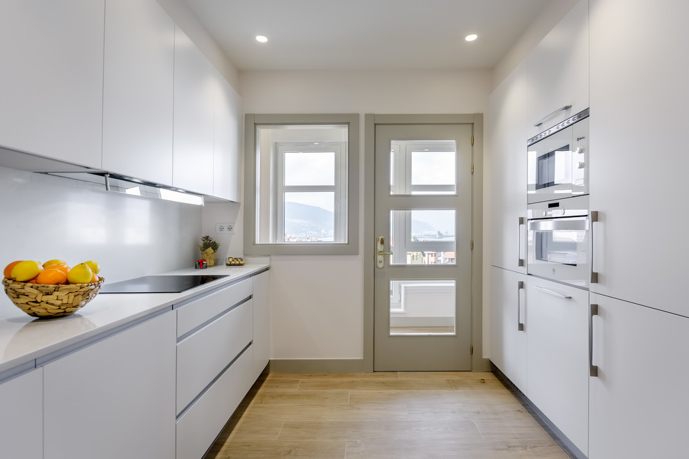 Réalisation d'une cuisine minimaliste avec un placard à porte plane, des portes de placard blanches, une crédence blanche et un plan de travail blanc.