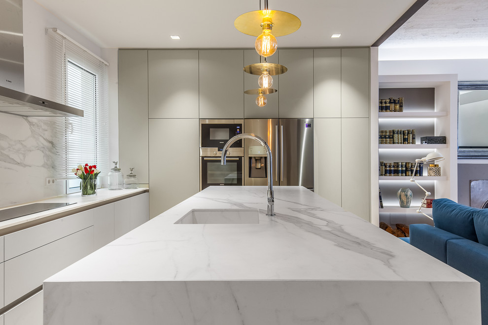 Modern inredning av ett stort linjärt kök med öppen planlösning, med en integrerad diskho, släta luckor, vita skåp, vitt stänkskydd, rostfria vitvaror och en köksö