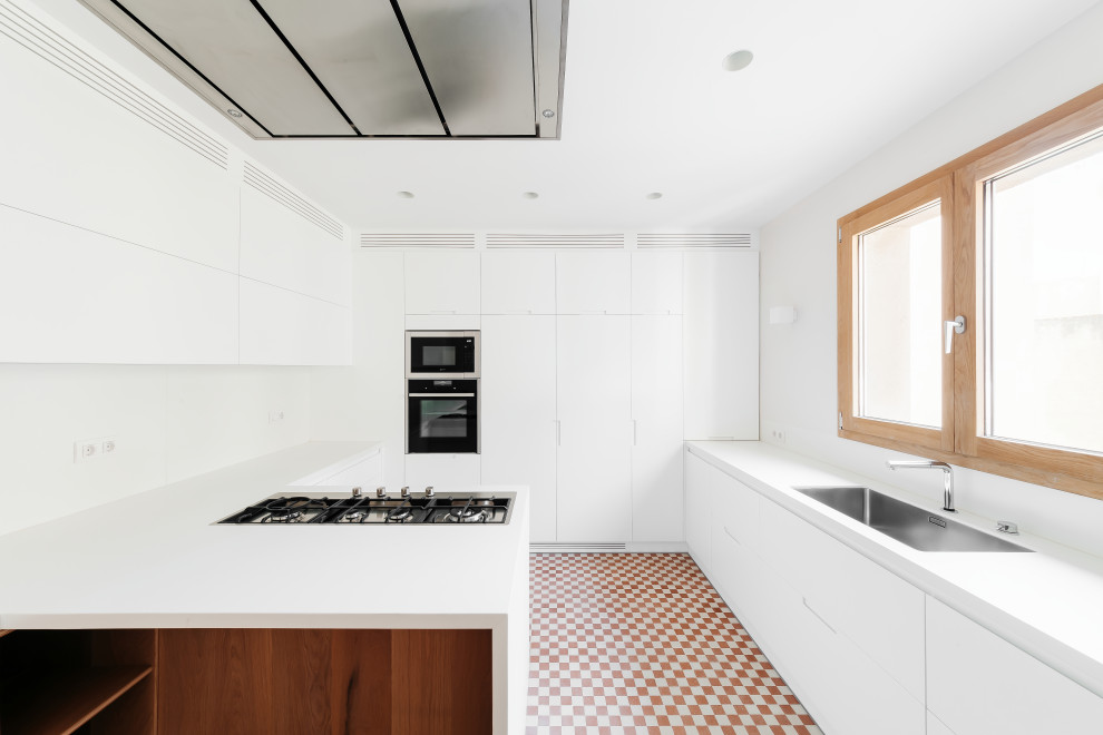 Idéer för ett avskilt, stort modernt vit u-kök, med en undermonterad diskho, släta luckor, vita skåp, bänkskiva i kvarts, vitt stänkskydd, rostfria vitvaror, klinkergolv i terrakotta, en halv köksö och flerfärgat golv
