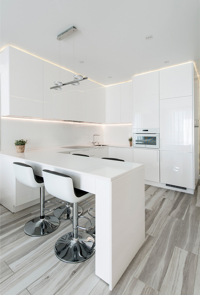 Design ideas for a medium sized contemporary u-shaped open plan kitchen in Palma de Mallorca with a single-bowl sink, flat-panel cabinets, white cabinets, white splashback, white appliances, medium hardwood flooring, a breakfast bar and white worktops.
